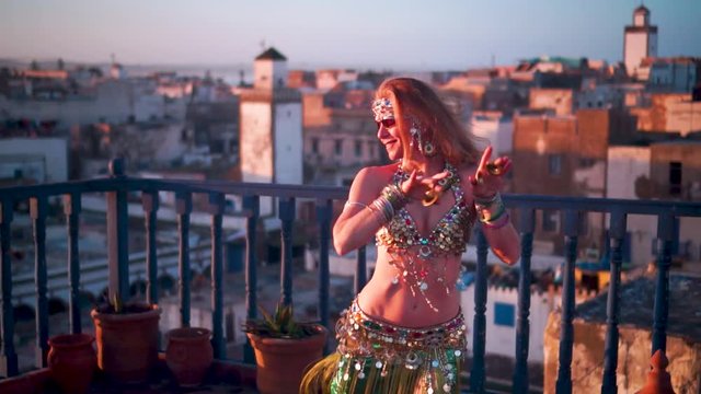 Smiling belly dancer with sunglasses performing on a rooftop at sunset in Essaouira, Morocco.