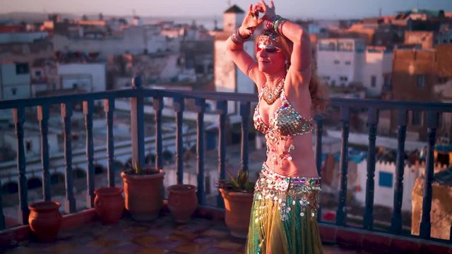 Beautiful belly dancer doing hip thrusts at sunset performing on a rooftop in Morocco.
