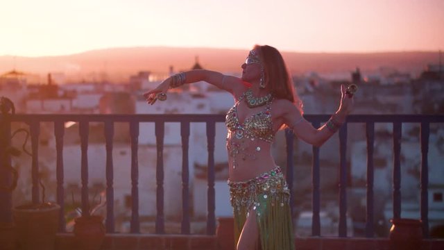 Beautiful belly dancer doing snake arms at sunset performing on a rooftop in Morocco.