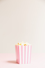 Popcorn bag with white and pink stripes at the light neutral backdrop. Empty minimalistic background. Romantic movie night and snack concept. Vertical