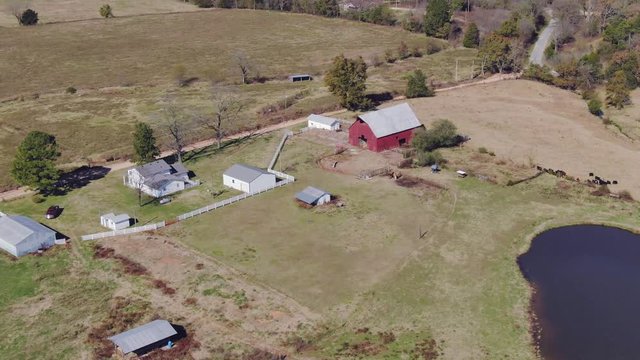 panning orbital aerial view of ranch house and barn with cow pond