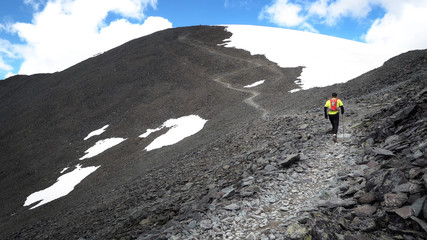 A runner on the trail climbing a stone path to the top of the mountain. Ultra trail running, sporting events, mountain trails marathon. © Nick Vakhrushev