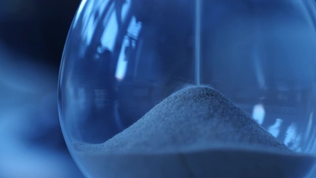 Hourglass sand falling in slow motion blue