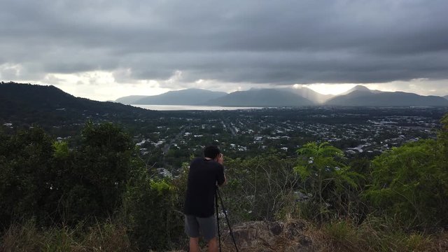 Photographer set up to take morning sunrise photos as the sun lifts above the mountain and shines down through the clouds.