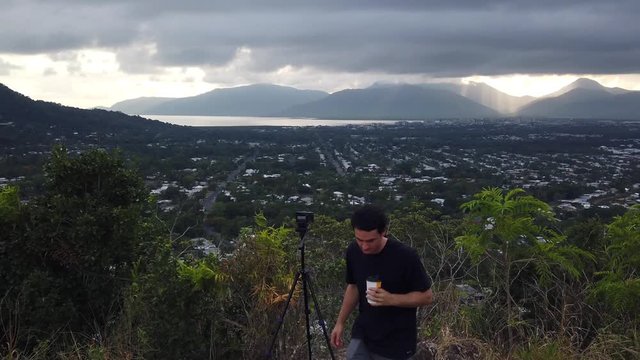 Photographer on top of a hill for photo shoot, drinking coffee watching the sun come up over the mountains between the clouds