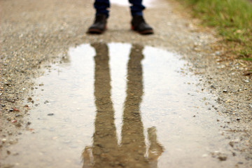 土手道の水たまりに映るブーツとジーンズを履いた男性