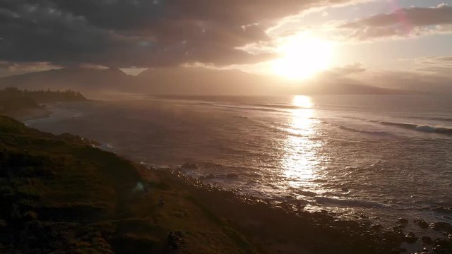 A drone flies along the coast of Maui Hawaii's Ho'okipa beach capturing images of the rocks and waves at sunset near Paia.