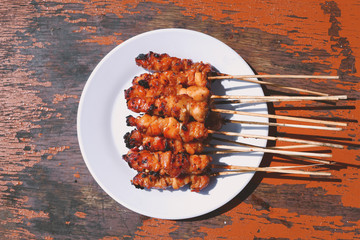 Chicken Satay or Chicken skin satay with red spices on white plate isolated on wooden tables 