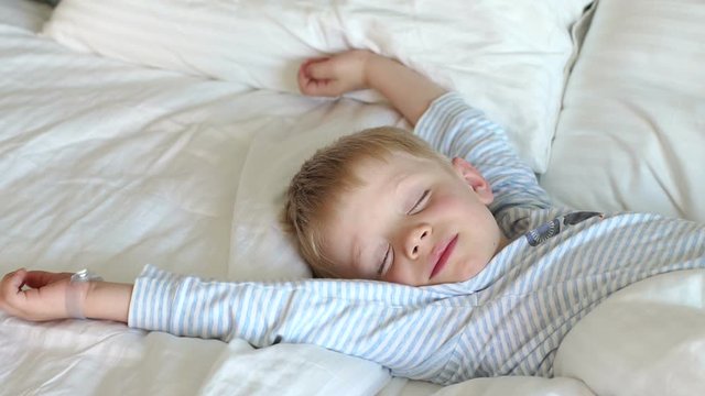 Little cute sleepy boy 5 years old wakes up in the morning in bed, he stretches out and slowly opens his eyes. Close-up. Slow motion.