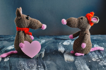 Handcrafted amigurumi rat standing opposite to the other one and holding pink heart. Valentine day, February 14, love, relations concept