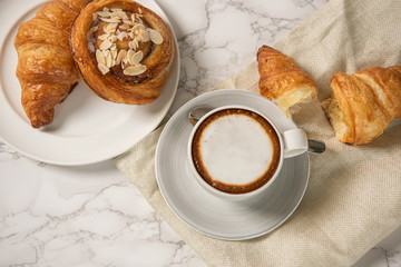 freshly baked croissants and pastry with a cup of coffee on marble table, top view