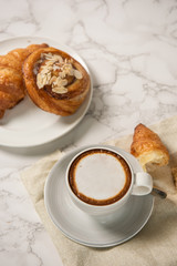 freshly baked croissants and pastry with a cup of coffee on marble table, top view
