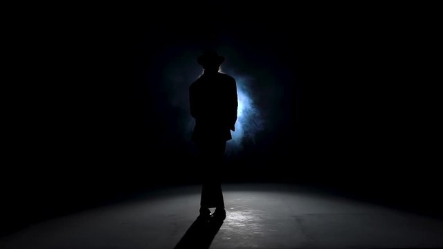 Silhouette of a young man dancer dancing in style Michael Jackson on a blue background of smoke. Close up, slow motion.