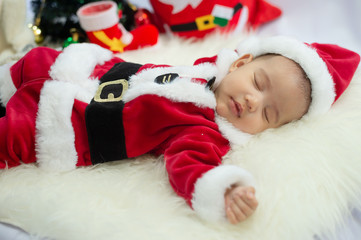 baby girl wearing red Santa Claus costume sleep on white fur carpet. Concept of celebrates Christmas and New Year's holidays.