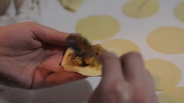 Making tradtional polish dumplings - woman stuffing dough for dumplings with sauerkraut and mushrooms using tablespoon. Polish christmas cuisine.