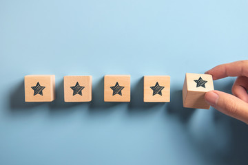 Man Hand putting wooden five star shape on blue background. Best Excellent Services Rating customer...