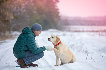 A human and dog are best friends. The man with the dog sitting in a snowy field in winter. Trained...