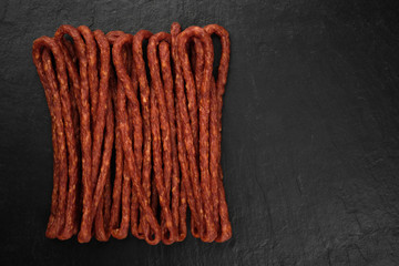 long and thin sausages kabanos on black stone background, isolated