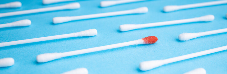 Blood on the hygiene cotton stick. Skincare mockup for design. Menstruation. Stack of disposable cotton stick on a blue background. Cosmetology concept. Bloody wound. Injury.