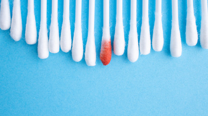 Blood on the hygiene cotton stick. Menstruation. Skincare mockup for design. Stack of disposable cotton stick on a blue background. Cosmetology concept. Bloody wound. Injury.