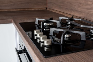 A modern gas cooker with ceramic hob, electric oven and a dark brown wooden kitchen ready for cooking a meal