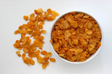 Corn flakes, dry, in a white bowl on a white cardboard surface.