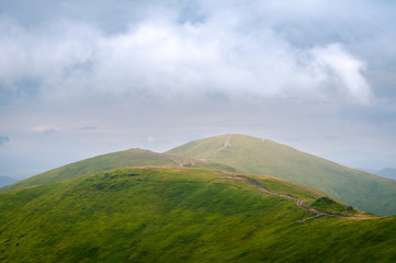 Fototapeta premium Beautiful mountain landscape with clouds. The road on the green top of Mount Ghimba in the Carpathians.