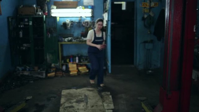 The concept of gender equality. A pretty young woman in a work uniform, working at the machine, the frame blurs, and then comes and wipes her hands, face close-up. Auto shop in the background