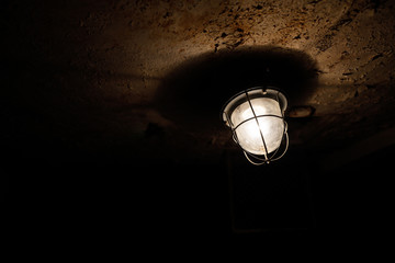 Grungy image with the light bulb and a metallic net on a worn out ceiling in an old prison cell.