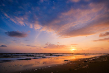Beautiful cloudscape over the sea with soft wave of blue ocean on sandy beach during sunrise.