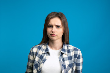 Fototapeta premium Front view of sad young woman looking at camera isolated on blue background
