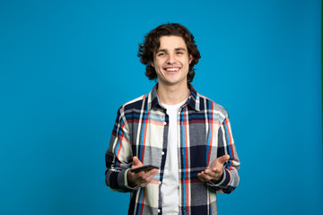 Front view of smiling young man holding smartphone and looking at camera