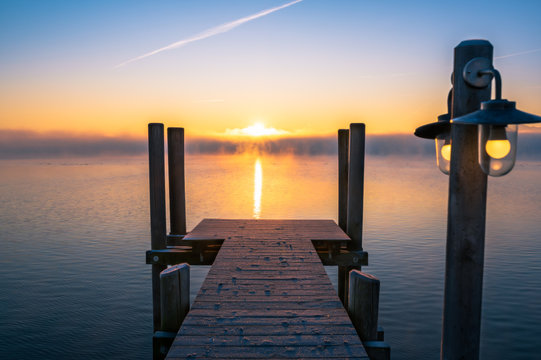 Steg am nebligen Chiemsee beim Sonnenaufgang im Dezember