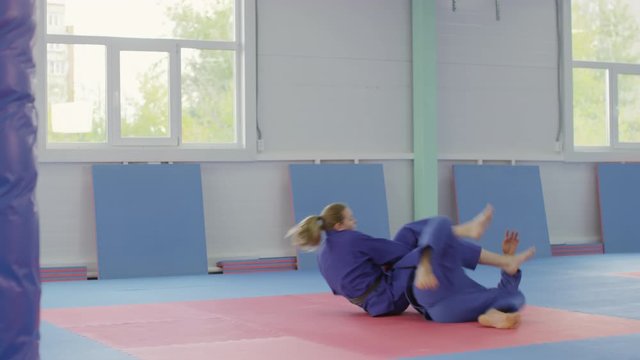 Tilt down shot of barefoot male and female martial art fighters in blue sports uniform practicing jiu-jitsu in gym