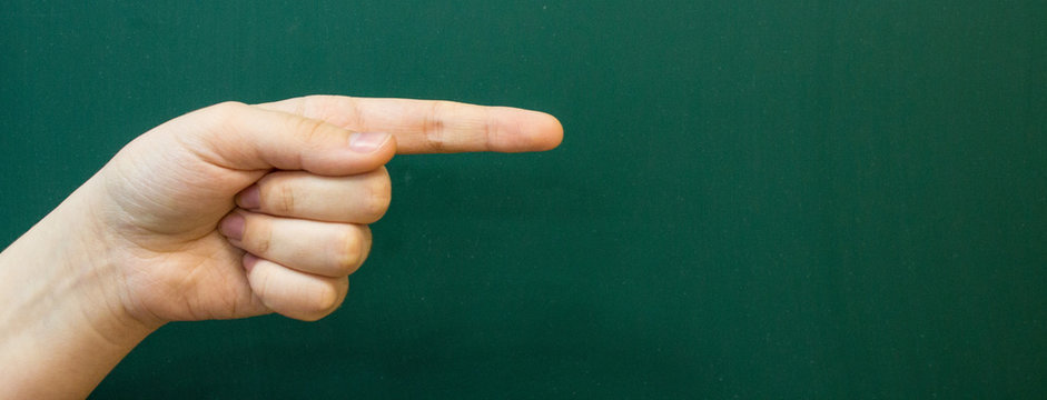 The hand of a teenager with an outstretched index finger on the background of a green chalkboard