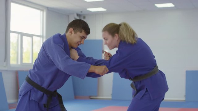 Young male and female combat athletes in blue jujitsu uniform talking and practicing takedown while training together in gym
