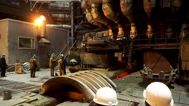 Rear view of two engineers looking at the giant blast furnace at the metallurgical plant, heavy industry concept. Stock footage. Two male workers inside the factory hot shop.