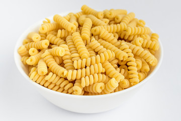 Dried fusilli Italian pasta in a round bowl ready to be cooked, isolated on a white table, side view of healthy food