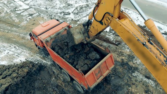A construction excavator loads a truck with sand and stones.