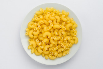 Dried cornetti rigati Italian pasta displayed in a white plate on a table, ready to be cooked, isolated on white background, top view or flat lay photograph of healthy food 