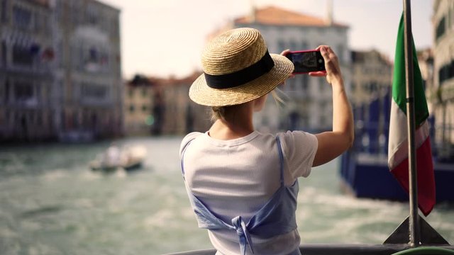 Positive female traveller floating on boat around Venice city taking panoramic images for creating publication in social network with content about journey to Italy during summer vacations.Sightseeing