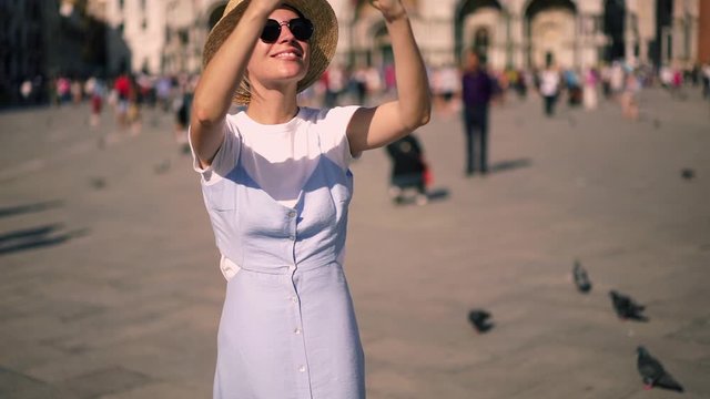 Slow Motion effect of young attractive female taking pictures of architecture buildings and after texting message in mobile phone sharing content. Woman walking on town street during summer vacations