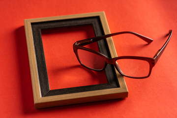 Spectacles and empty photo frame against red background