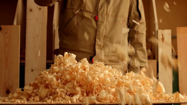 Joiner with bristle brush throw about big heap of effect wood sawdust in the carpentry
