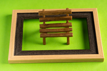 Miniature bench and empty frame against green background
