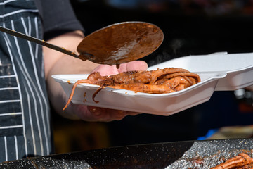Cooked octopus with tomato sauce being transferred to a take away box at a street food festival,...