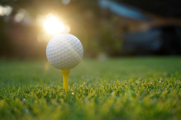 Golf ball on tee in beautiful golf course at sunset background.