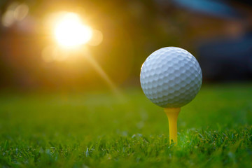 Golf ball on tee in beautiful golf course at sunset background.
