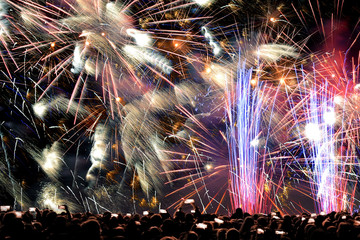 Colorful festive salute at city festival. People watching the fireworks. New Year's Eve concept. Explosions of colorful abstract lights