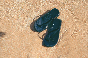 Black flip flops on sand in the beach sea